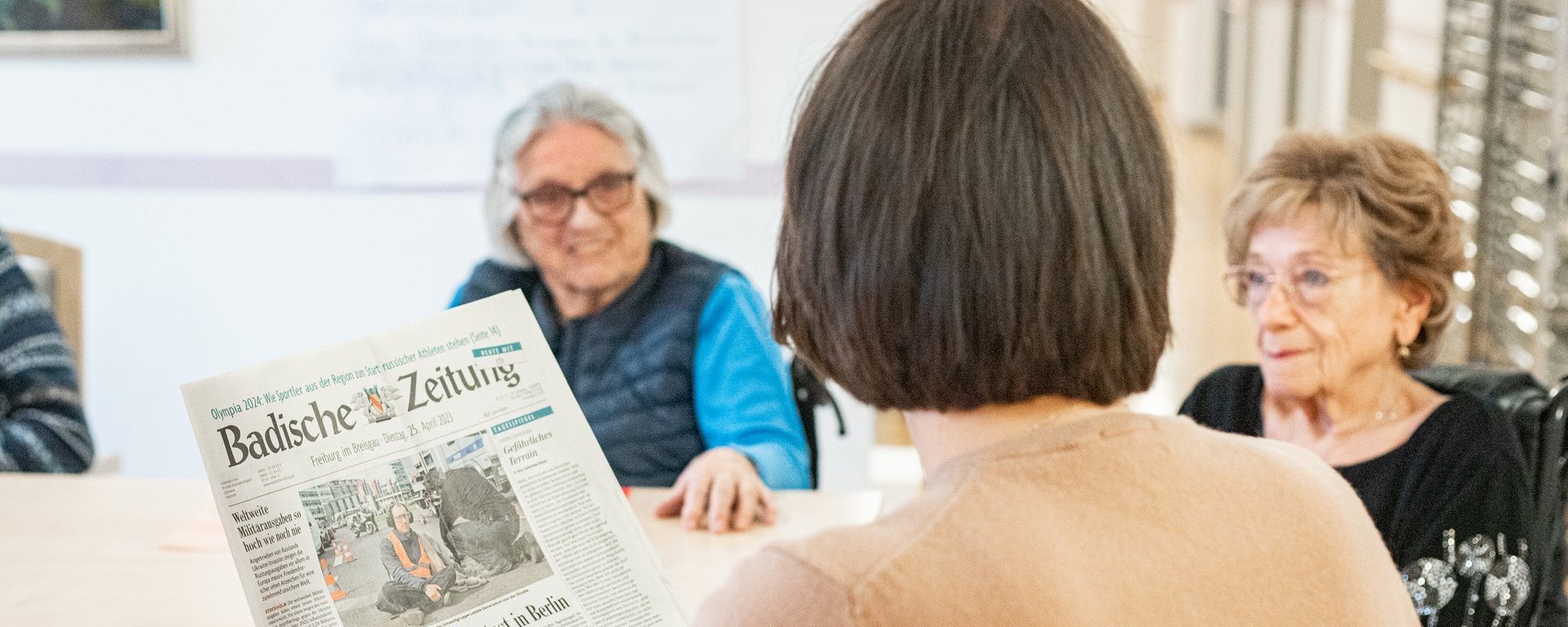 Eine Betreuerin liest Senioren die Zeitung vor