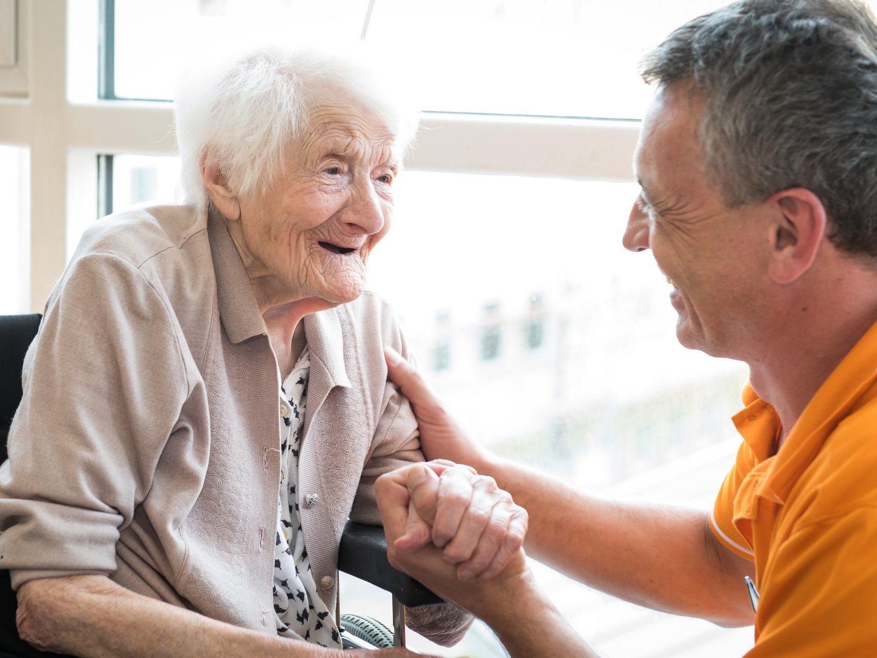 Ein Pfleger hält die Hand einer Bewohnerin - beide lachen