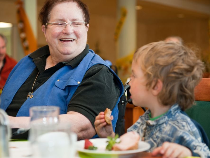 Kinderbesuch im Altenheim: ein kleiner Junge isst gemeinsam mit einer Bewohnerin im Speisesaal