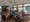 Ein Gruppenbild in einem hellen Restaurant: Viele Menschen sitzen an langen Tischen, essen und unterhalten sich gesellig bei Tageslicht.