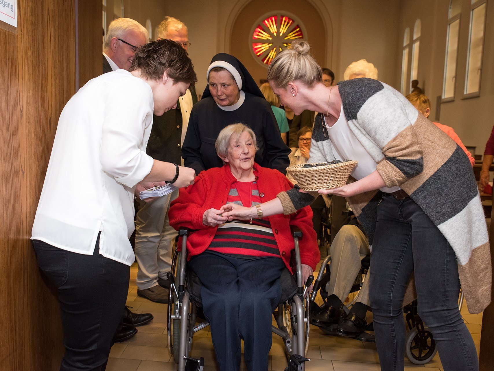 In der Kirche: eine Frau im Rollstuhl wird von einer Schwester zum Ende der Messe hinausgeschoben