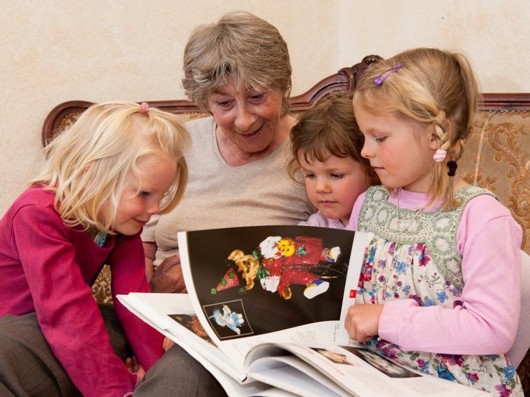 drei kleine Mädchen sitzen mit einer Bewohnerin auf einem Sofa und sehen gemeinsam ein Buch an