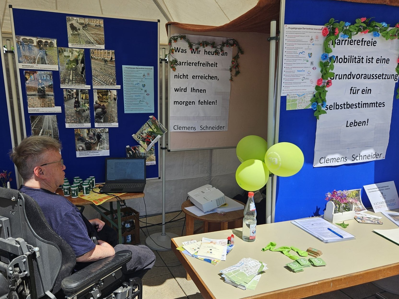 Ein Mann im Rollstuhl betrachtet einen Infostand zur barrierefreien Innenstadt Freiburgs.