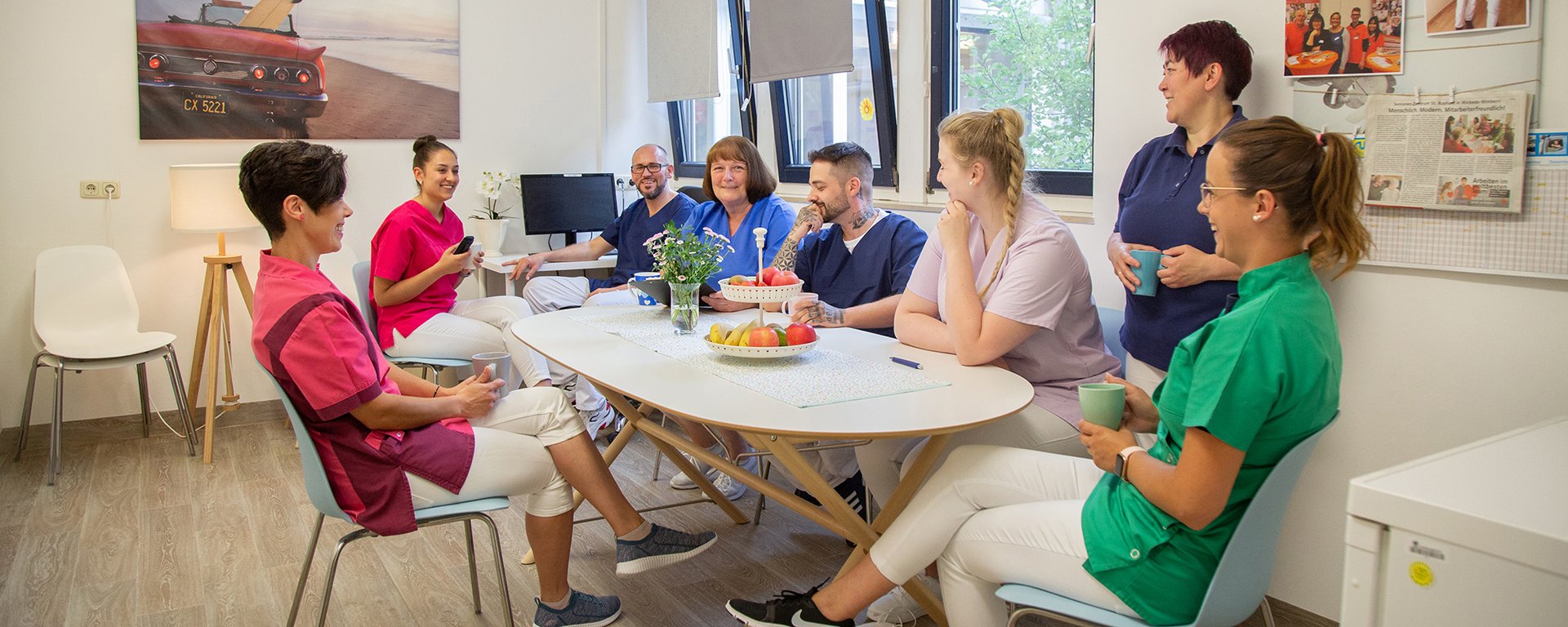 Eine Gruppe Pflegekräfte sitzen um einen Tisch im Aufenthaltsraum, sprechen und lachen